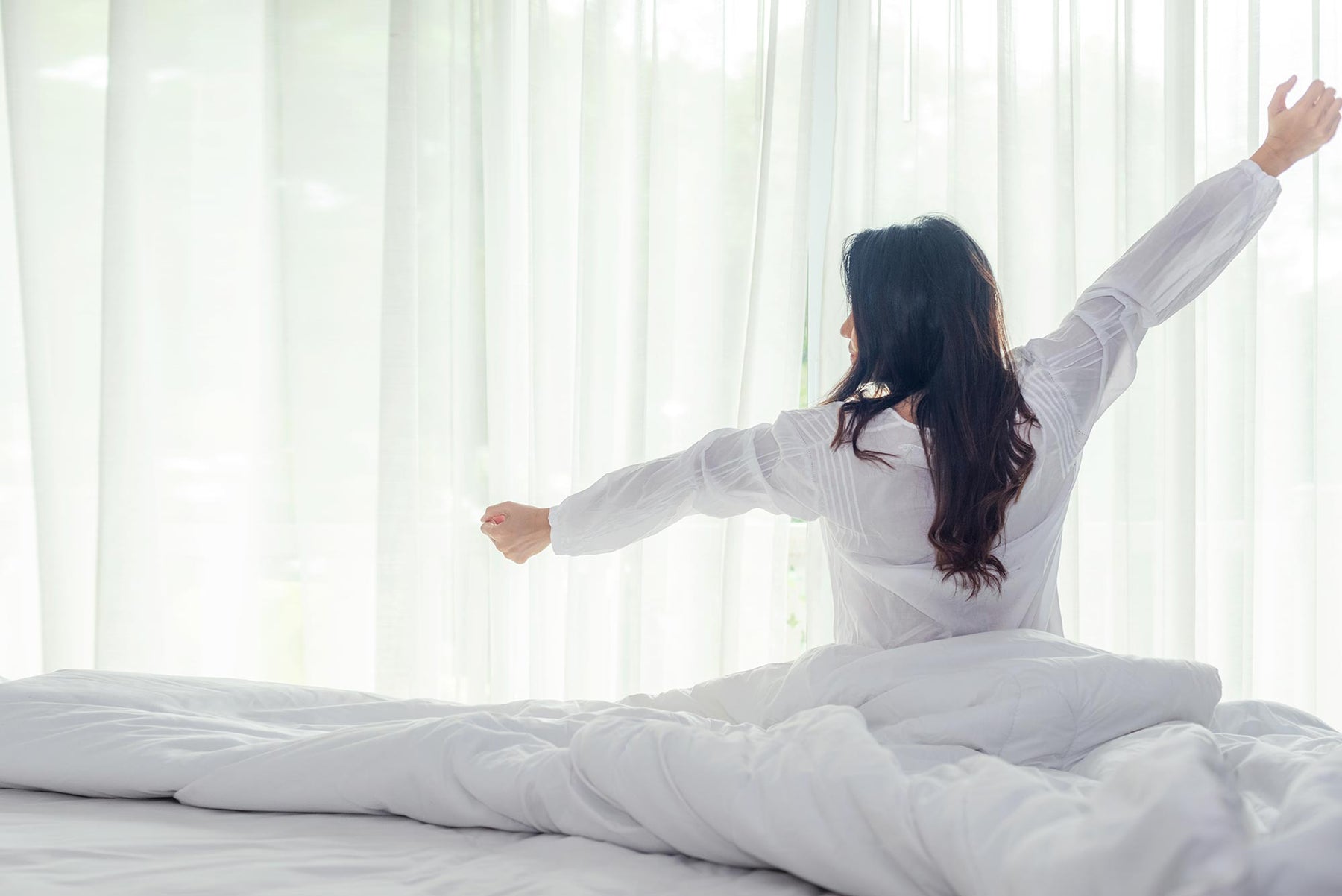 Woman waking up from sleep. Duvet, mattress and curtain in background.