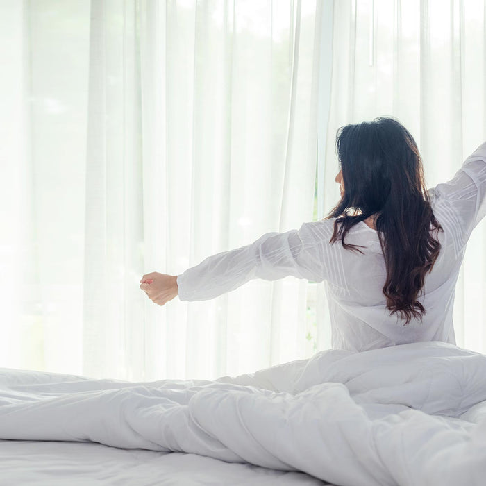 Woman waking up from sleep. Duvet, mattress and curtain in background.