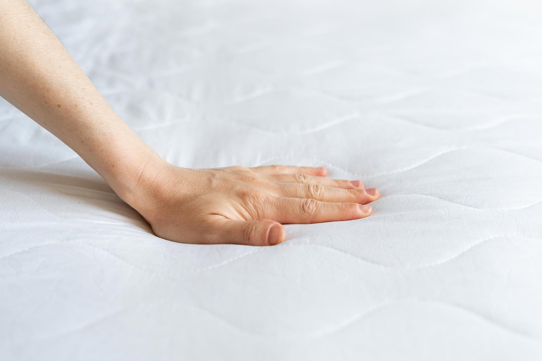 A hand pressed on a mattress.
