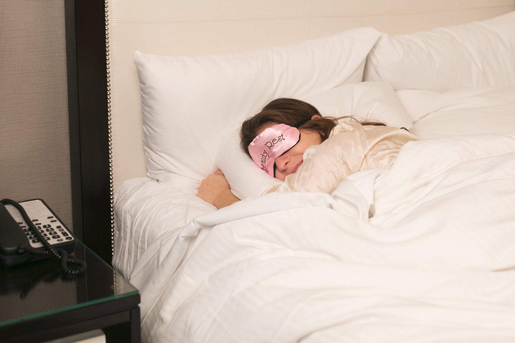Woman Sleeping with Pink Sleep Mask, Large Comfy Bed in Neutral Coloured Room