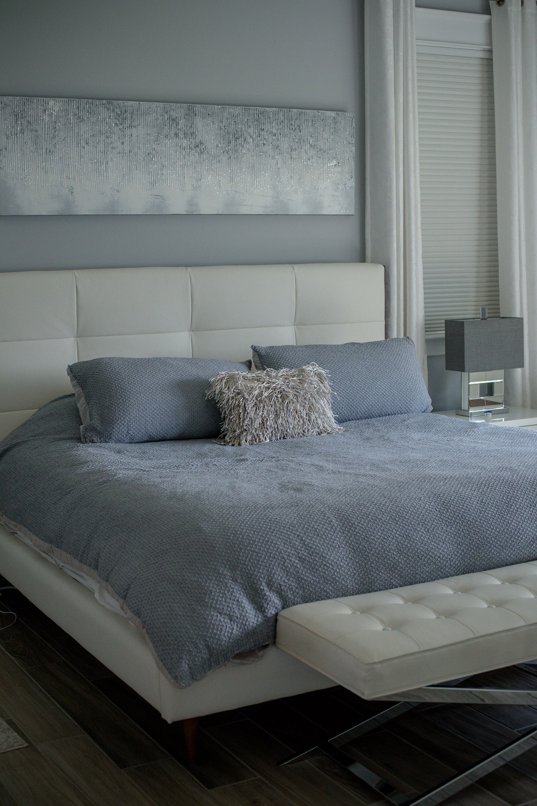 Large Bed Covered in Grey Sheets and Pillows in Large Neutral Coloured room with Curtains