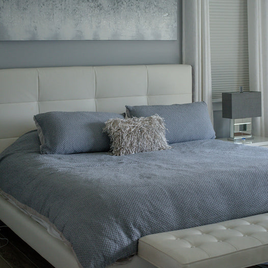 Large Bed Covered in Grey Sheets and Pillows in Large Neutral Coloured room with Curtains